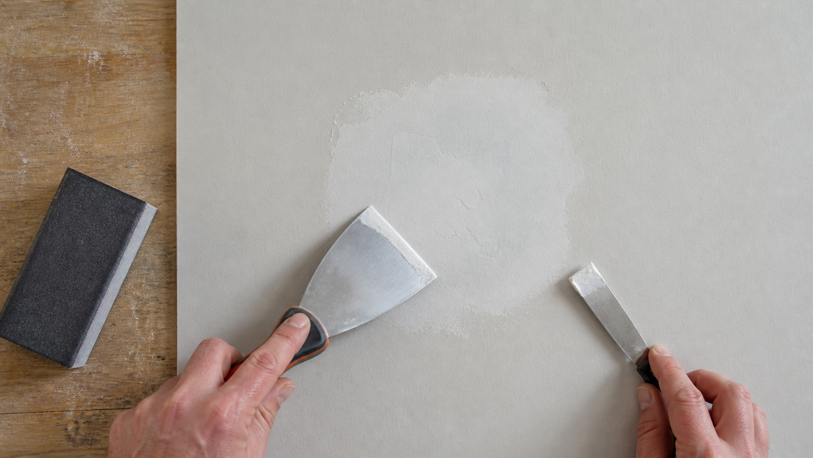 Application d’une fine passe d’enduit avec un couteau large sur un mur en plaque de plâtre